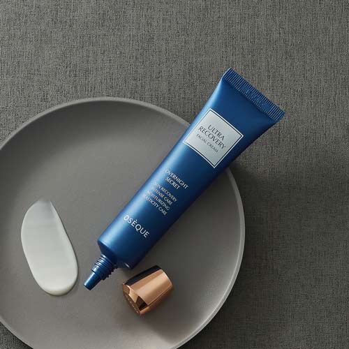 회색 원형 접시 위에 놓인 오제끄 블루 튜브형 크림과 질감 샘플 A blue tube of Oseque facial cream with a smear of product on a grey dish