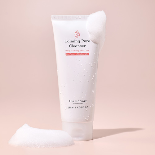 부드러운 거품과 함께 촬영된 더 하르나이 칼밍 퓨어 클렌저 Calming cleanser tube with water droplets and soft foam on pink background