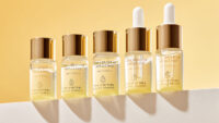 황금빛 배경 앞에 줄지어 선 유자C 브라이트 업 앰플 제품 이미지 Lineup of The Harnay’s Yuja C ampoule bottles under golden light