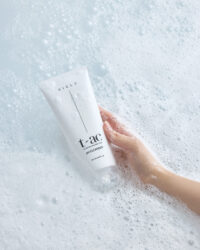 하얀 거품 위로 손이 제품을 부드럽게 감싸 쥐고 있는 클렌저 연출 이미지 A soft human hand holds the Vicle cleanser tube among thick, airy foam