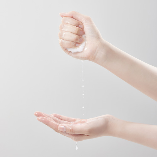 한 손으로 적신 패드를 꽉 쥐고 다른 손바닥 위로 물방울이 떨어지는 장면 A soaked cotton pad squeezed in one hand as water drips into the other
