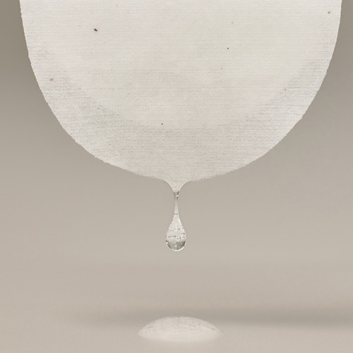 패드 하단에서 떨어지는 투명한 액체 방울과 바닥에 맺힌 자국의 정적인 장면 A close-up image of liquid drop falling from a skincare pad with minimal composition
