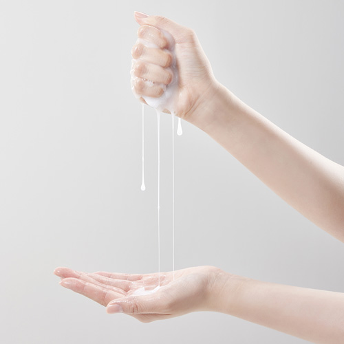 손으로 유백색 제형을 짜내며 다른 손에 떨어뜨리는 장면 A hand squeezes a white milky skincare product into the open palm of the other hand