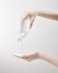 한 손으로 토너 용기를 잡고 다른 손 위의 패드에 액체를 붓는 장면 A visual of Vicle toner being poured from one hand onto a pad held by the other