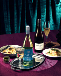 두 병의 화이트 와인과 파스타 요리가 어우러진 정갈한 테이블 연출 이미지 A composed table setting with two bottles of white wine, pasta dishes, and elegant props on deep-toned fabric