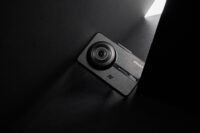 어두운 배경과 날카로운 빛 속에 비스듬히 놓인 IROAD NX1000 블랙박스 제품 사진 An angled IROAD NX1000 dash cam lit by a sharp slit of light against a deep black background.