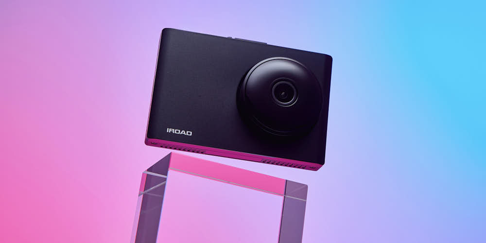 블루와 핑크 그라데이션 조명 아래 아크릴 받침대 위에 떠 있는 아이로드 NX1000 블랙박스 제품 사진 Photo of IROAD NX1000 dashcam floating above acrylic block with blue and pink gradient lighting