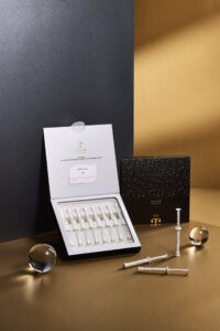JenaCell 시린지 형태 세럼 제품이 블랙과 골드 패키지와 함께 연출된 이미지 JenaCell syringe-type serum displayed with black and gold packaging