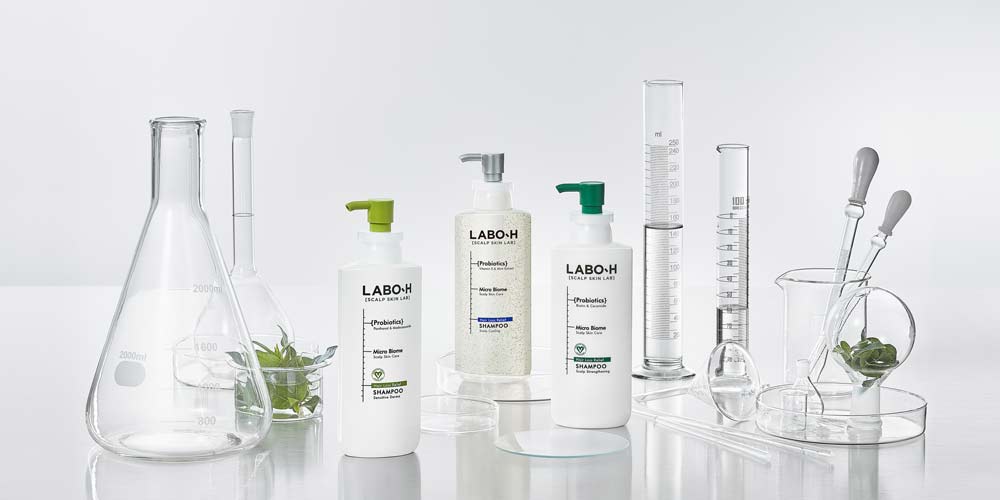 비커와 유리 기구 사이에 놓인 Labo-H 탈모 완화 샴푸 제품 사진 Labo-H shampoo bottle placed among glass beakers and lab props
