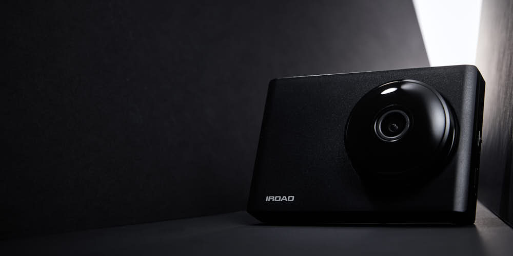 IROAD 블랙박스가 어두운 배경 속 강한 라이트와 함께 세련된 디자인으로 표현된 제품 사진 IROAD Blackbox displayed in a dark minimal setup with strong directional light emphasizing its sleek design