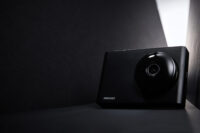 IROAD 블랙박스가 어두운 배경 속 강한 라이트와 함께 세련된 디자인으로 표현된 제품 사진 IROAD Blackbox displayed in a dark minimal setup with strong directional light emphasizing its sleek design