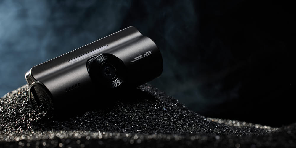 검은 모래 위에 놓인 아이로드 블랙박스 X6 제품 사진 IROAD Dashcam X6 placed on black sand surface