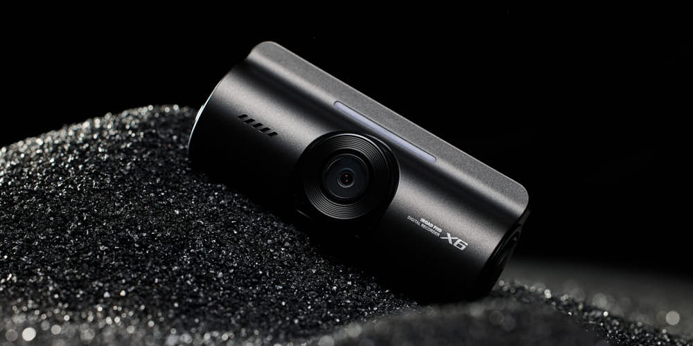 블랙 샌드 위에 놓인 아이로드 X6 블랙박스 제품 사진 IROAD X6 dashcam on black sand texture