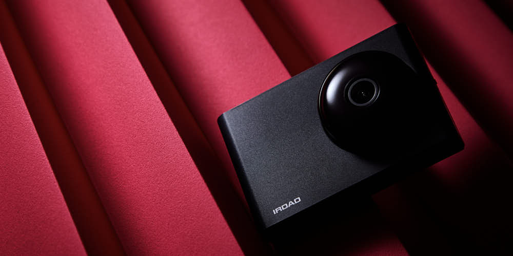 보라, 핑크, 블루 조명이 어우러진 배경에 놓인 아이로드 NX1000 블랙박스 iroad NX1000 dashcam against purple, pink, and blue light background