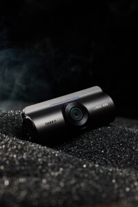 블랙 텍스처 위에 배치된 아이로드 X6 블랙박스 제품 사진 IROAD X6 dashcam placed on black sand textured surface