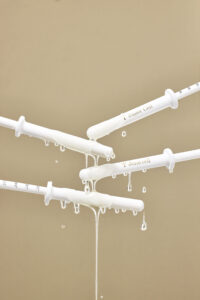 제나셀 세럼 주사기에서 흐르는 금빛 제형 클로즈업 사진 Close-up shot of JenaCell serum syringe with golden liquid flowing, styled in a lab-inspired concept